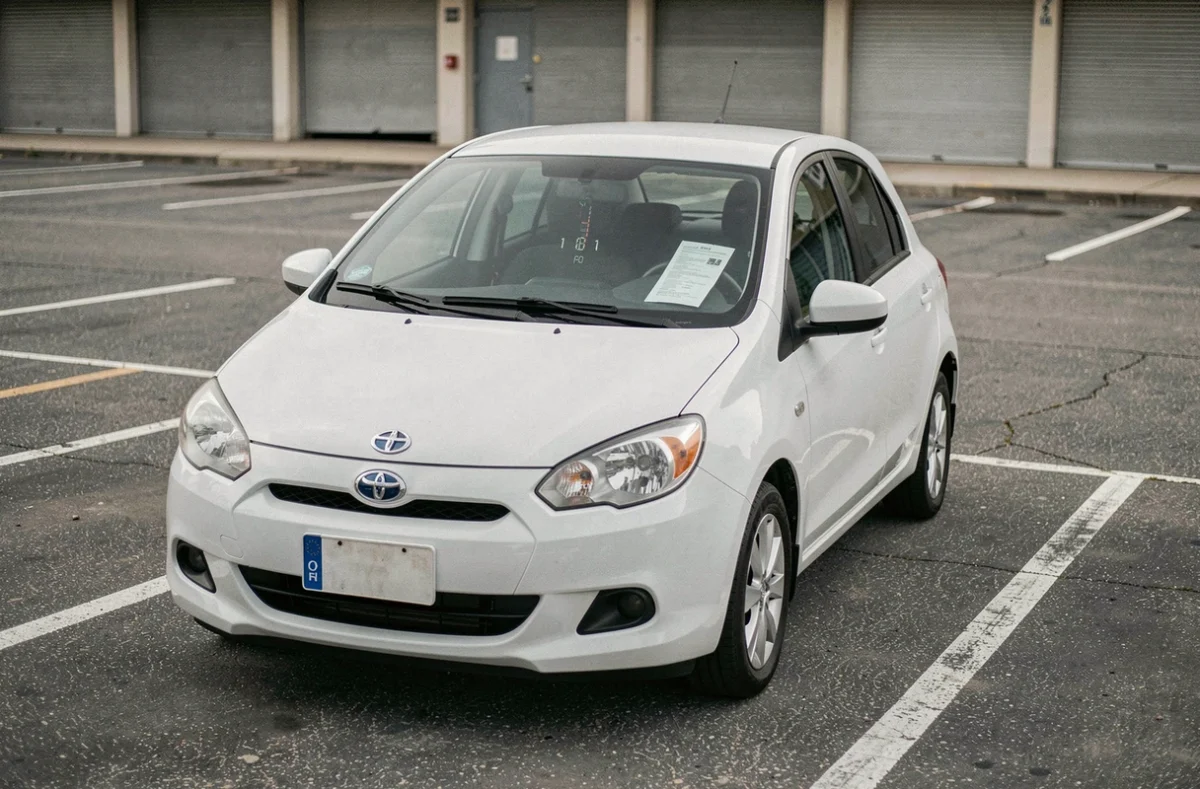 Petite voiture citadine garée avec un document d'assurance kilométrique sous l'essuie-glace dans un parking vide